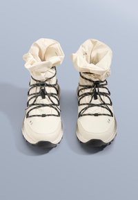 Beżowe buty outdoorowe z teksturowaną, wodoodporną cholewką z tkaniny, elastycznym kołnierzem i czarnymi sznurówkami zapewniającymi pewne dopasowanie. Czarna gumowa podeszwa.