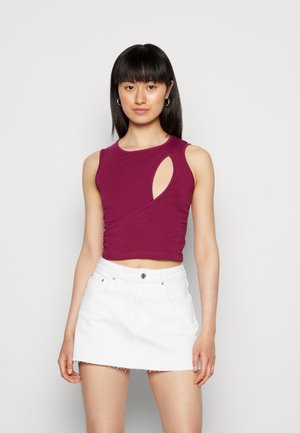 Top roxo sem mangas com um design recortado, apresentando uma silhueta ajustada e textura suave, combinado com uma saia mini de denim branca.