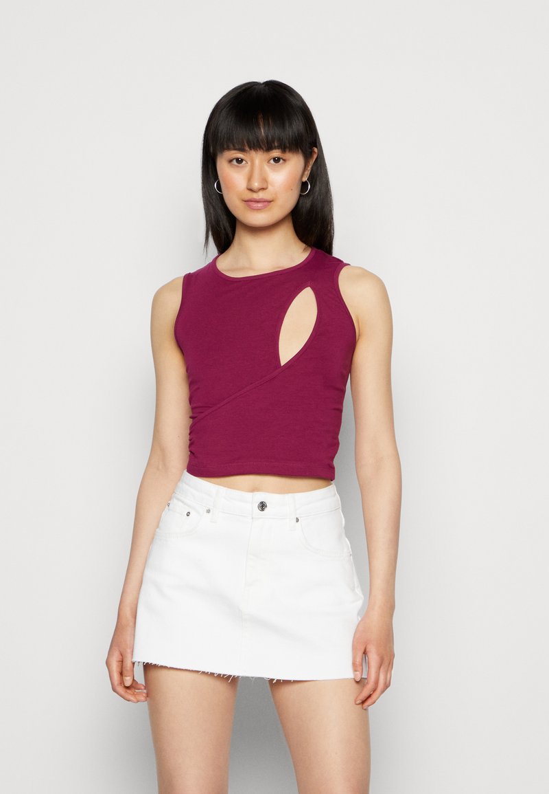 Top roxo sem mangas com um design recortado, apresentando uma silhueta ajustada e textura suave, combinado com uma saia mini de denim branca.