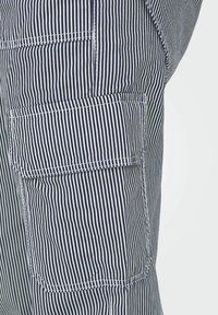 Marinblå och vita randiga cargo-byxor med sidoficka. Tyget verkar lätt och har märkbara sömnadsdetaljer och textur.