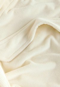 Țesătură crem cu textură, având nervuri verticale fine și o senzație moale și pufoasă, așezată în falduri delicate.