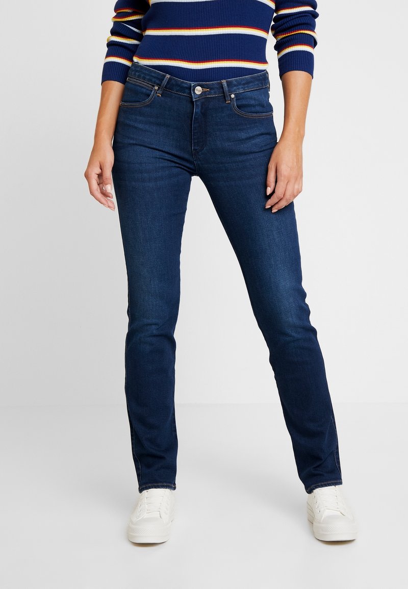 Jeans ajustados azul oscuro en tejido de mezclilla, con un diseño clásico de cinco bolsillos, botón de metal y detalles de costura sutiles.