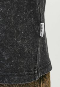 Sort kortærmet T-shirt med en struktureret finish, prydet med et sidetags mærket "ORIGINALS." Enkel design med subtile farvevariationer.