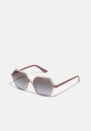 Óculos de sol hexagonais com lentes cinza em degradê, armação transparente em tom rosa e hastes finas em rosa com o logotipo "vogue".