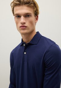 Marineblaue Langarm-Polohemd aus weichem Stoff mit klassischem Kragen und Knopfleiste mit zwei Knöpfen. Verfügt über ein minimalistisches Design ohne Muster.