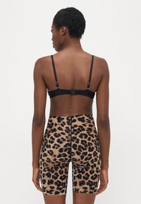 Black bra with adjustable straps, paired with high-waisted shorts featuring a leopard print on a tan background. Smooth texture, form-fitting design.