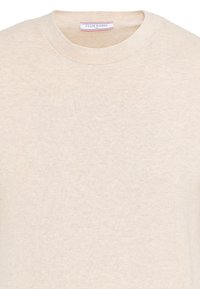 Pull beige à col rond avec une petite étiquette en tissu à l'intérieur du col indiquant "Felix Hardy M."