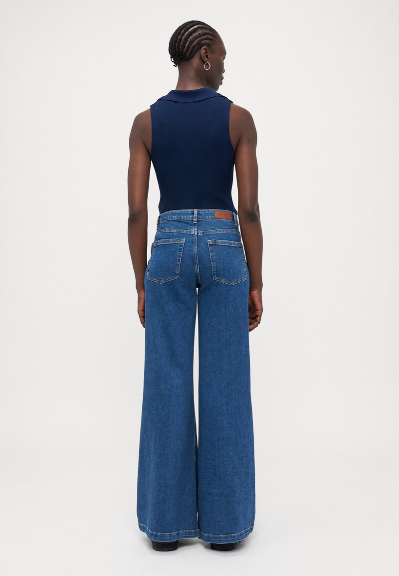 Haut sans manches bleu marine avec col, associé à un jean en denim bleu à jambes larges. Le jean a une taille haute et deux poches arrière.