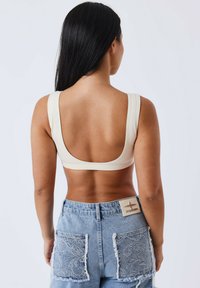 Romige geribbelde bralette met brede banden en een lage rug. Gepaard met lichtblauwe denim shorts met kanten zakken en een decoratieve hardwareaccent.