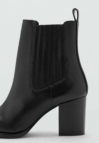 Botín de cuero negro con paneles laterales elásticos, tacón de bloque y textura lisa. Cuenta con una tira en la parte trasera para facilitar su colocación.