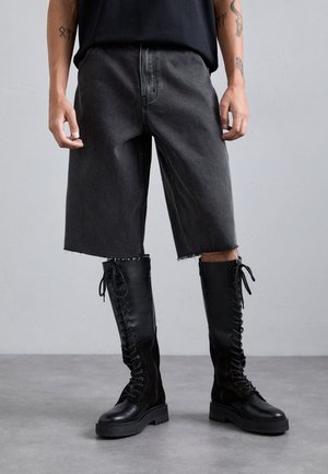 Black denim shorts with frayed hems, paired with tall black lace-up boots featuring a mix of leather and suede textures.