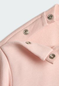 Světle růžová bavlněná tkanina s texturovanou vazbou, s kovovými patentkami na rameni pro snadné zapínání.