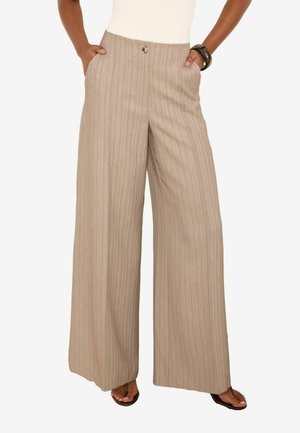 Femme portant un pantalon beige taille haute à jambes larges avec des rayures verticales, les mains dans les poches, associé à des sandales foncées et un bracelet sombre.