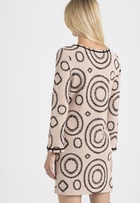 Vestido corto rosa con mangas largas que presenta diseños circulares negros y bordes en zigzag. Textura acanalada con un estilo ajustado.