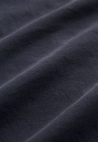 Tissu gris foncé avec une texture subtile, présentant une surface lisse et douce, plié en vagues pour révéler profondeur et douceur.