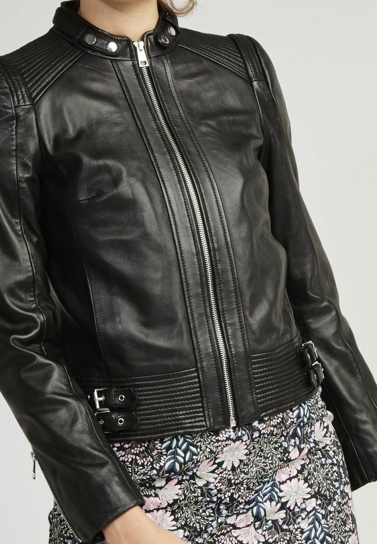 Femme portant une veste en cuir noir style motard avec fermeture éclair et détails de boucle sur une jupe à motif floral.