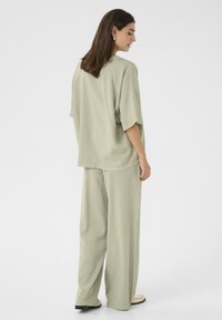 Brīvi pieguļošs, gaiši zaļš apģērbs, kas sastāv no īsām piedurknēm topa un platām biksēm, izgatavots no gludas auduma ar ikdienišķu krāsojumu.