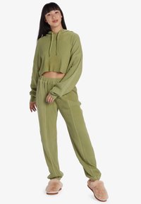 Lichtgroene, geribbelde cropped hoodie met lange mouwen en een trekkoord, gecombineerd met bijpassende losse broek; model draagt fuzzy beige pantoffels.
