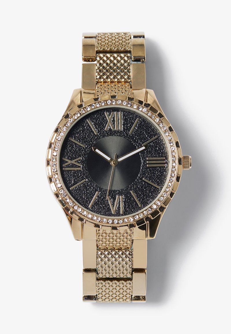 Montre dorée avec un cadran noir texturé, des chiffres romains et une lunette ornée de cristaux. Elle possède un bracelet en maille et un boîtier rond.