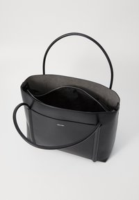 Borsa a mano in pelle nera con una texture liscia, chiusura con zip, doppi manici e un rivestimento interno morbido. Presenta un logo sul davanti.