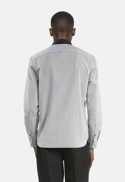 Camisa de manga larga a rayas en gris y blanco con cuello negro. Presenta puños abotonados y un dobladillo curvado. Textura de tela suave.