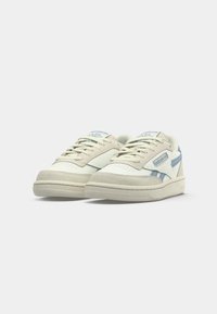Bež i svijetlo plave Reebok tenisice s vezicama, suedinim detaljima i klasičnim logom s boka i jezika, prikazane sprijeda.