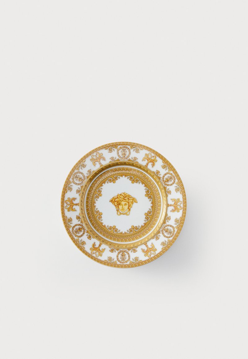 Bílý porcelánový talíř s propracovanými zlatými vzory a středovým znakem hlavy Medúzy, odrážející klasický luxusní design.