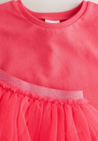 Camiseta rosa de algodón con una superposición de tul en el dobladillo. Textura suave con un cinturilla elástica brillante que acentúa el diseño.