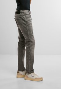 Blugi din denim gri, cu o croială relaxată, având accente uzate și un design cu picior drept. Asortați cu adidași albi și o cămașă neagră.