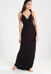 Vestido maxi negro con escote en V profundo, tirantes ajustables y detalle fruncido en la cintura. Fabricado con tejido suave y elástico.