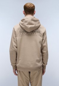 Sudadera beige con un estampado de logo texturizado en la parte posterior, con capucha ajustable y puños y dobladillo acanalados. Textura de tela suave.