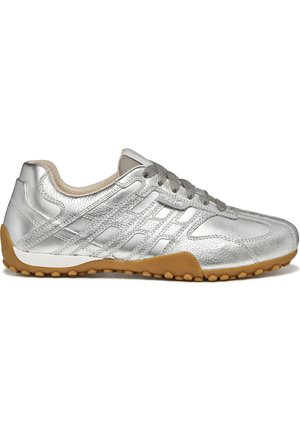 Zapatilla deportiva de cuero plateado texturizado con cordones grises y suela de goma color caramelo con pequeños tacos redondos de tracción, vista lateral sobre fondo blanco.