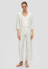 Lichtgroene cropped cardigan over een witte top, gecombineerd met hoge taille, wijde witte jeans en platte sandalen met een bandontwerp.