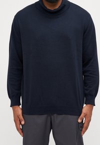 Pull à col roulé bleu marine en tissu doux et lisse. Comprend des manches longues, des poignets côtelés et une coupe classique avec une silhouette décontractée.