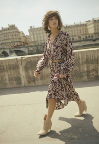 Lila Paisley-Muster Kleid mit langen Ärmeln und gerafften Manschetten, kombiniert mit beigen spitzenknöchelhohen Stiefeln und einem dekorativen Gürtel.