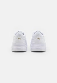 Baskets blanches de sport avec tige synthétique texturée, col rembourré, lacets plats et accents de logo doré sur le talon et le côté.