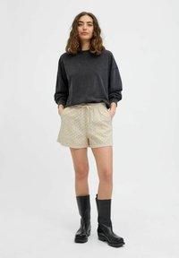 Dunkelgrauer, übergroßer Sweatshirt, beigefarbene Shorts mit Ösenmuster und schwarze Knöchelboots. Lässiges Outfit mit lockerer Passform und Kordelzugbund.