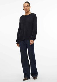 Donker, textuurvol gebreid sweater met een wijd halsline en verlaagde schouders, gecombineerd met hoge donkere denim broek en bruine laarzen.