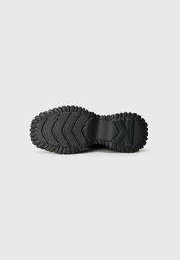 Black rubber shoe sole with a zigzag tread pattern, textured detailing, and a pronounced edge for grip and stability.