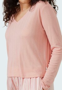 Ljust rosa V-ringad långärmad topp med vertikal ribbad struktur och små dekorativa detaljer. Tyget verkar mjukt, den avslappnade passformen kompletterar lagerpåsade stilar.
