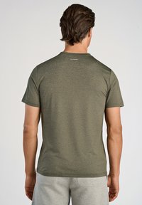 Oliwkowa koszulka z krótkim rękawem z teksturowanym wzorem, okrągłym dekoltem i małym logo z tyłu. Nosi ją z szarymi szortami.