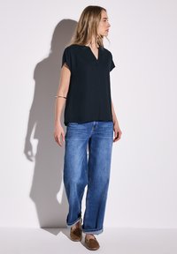 Top navy a maniche corte con scollo a V, abbinato a jeans azzurri larghi e scarpe slip-on marroni. Tessuto dalla consistenza liscia.