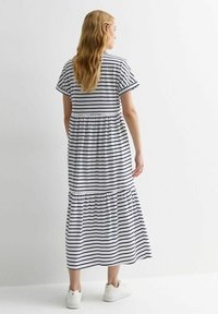 Gestreepte katoenen maxi-jurk met korte mouwen, witte basis, marineblauwe strepen, gathered taille en ruches aan de onderkant. Gecombineerd met witte sneakers.