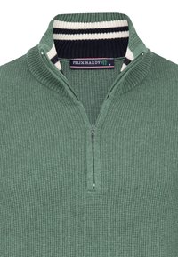 Grøn trøje med lynlås og struktureret strikmønster. Har en kontrasterende krave i navy og hvid striber, mærkat med mærke ved halsen.