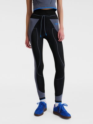 Kvinde iført sorte og grå leggings med blå accenter, matchende crop top, hvide sokker og klare blå sneakers.