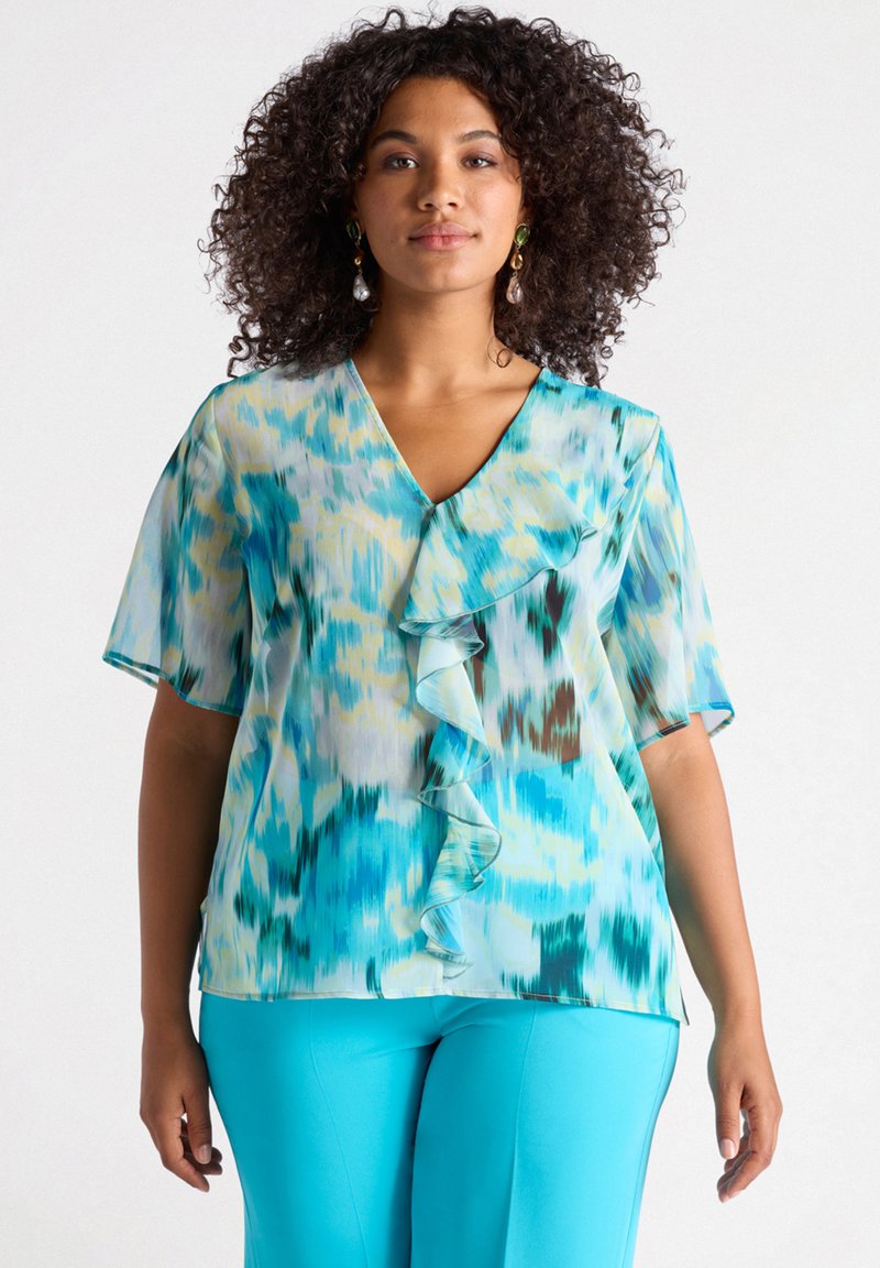 Blusa leggera con motivo blu e verde, colletto a V, frontale con volant e maniche corte, abbinata a pantaloni blu brillante.