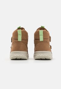 Bottines en daim marron avec des poignées vertes, dotées de deux sangles ajustables et d'une semelle en caoutchouc blanche tachetée.