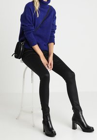 Maglione dolcevita blu lavorato a maglia, pantaloni neri aderenti e stivaletti neri con tacco alto; include una piccola borsa a tracolla nera.