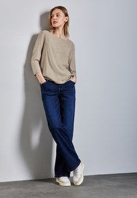 Hellbeige gemusterte Langarmbluse kombiniert mit dunkelblauen Jeans und hellen Sneakers. Die Jeans haben eine lockere Passform und ein gerades Bein-Design.