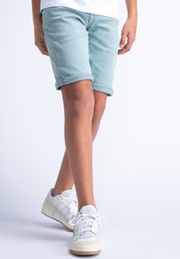 Pantaloni corti azzurri chiari con risvolto fatti di cotone, abbinati a sneakers bianche con tre strisce e una suola testurizzata.